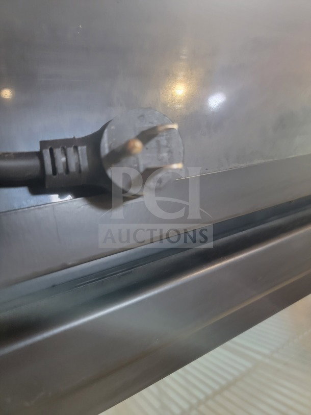 Close-up of the plug from a True GDM-49-HC commercial refrigerator, showing its prongs against a metallic background.