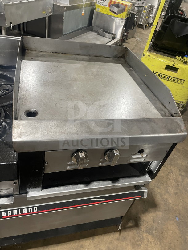 Garland stainless steel gas range with 6 burners, raised flat griddle, double oven, broiler, and overhead salamander shelf.