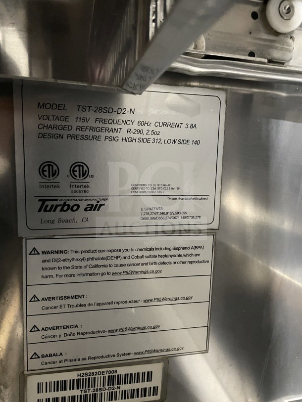 Turbo Air TST-28SD-D2-N refrigerated prep table, 115V, stainless steel, 2 drawers, on casters, label shows specs and warnings.