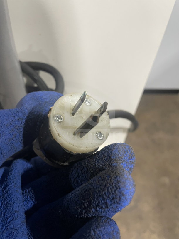Close-up of a power plug for the JAC MJL 450/13 bread slicer, showing a three-pronged design with a blue-gloved hand.