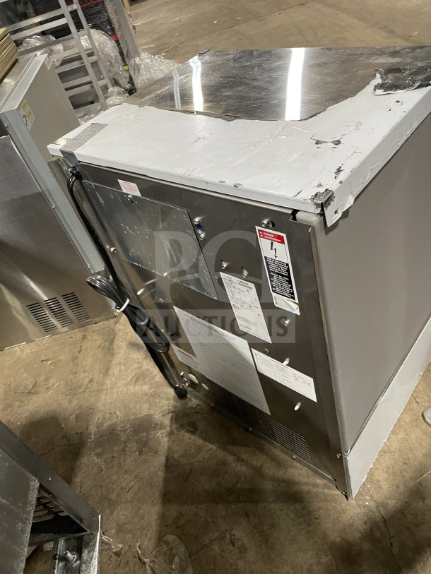 IceOMatic commercial under-counter ice machine, 115V, 1 phase, silver, visible wear on top, various labels, industrial setting.