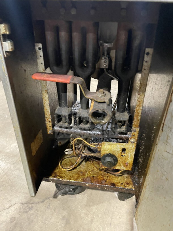 Commercial stainless steel gas-powered fat fryer with back splash, on casters. Visible wear and rust on interior components.