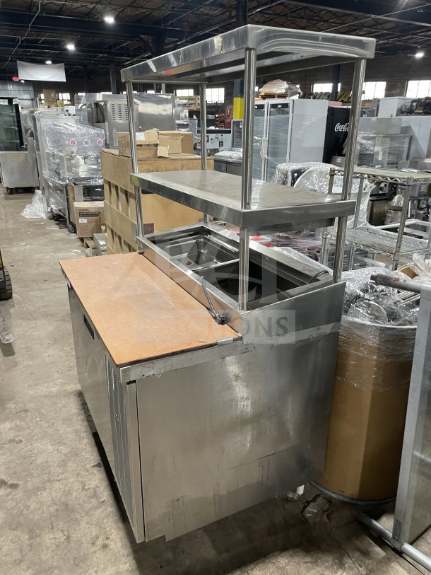 Delfield stainless steel pizza prep table with refrigerated base, double overhead shelf, chrome rack, and enclosed storage. 115V, 1 Phase.