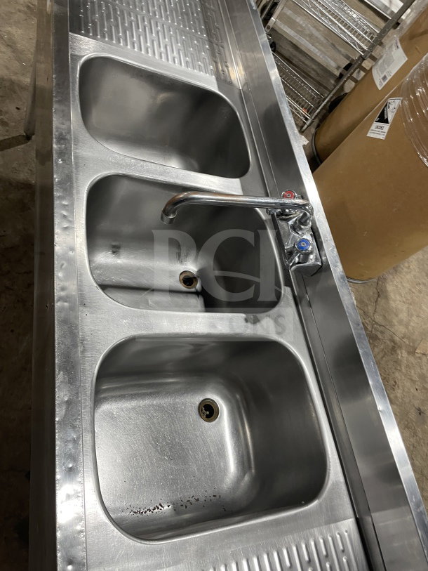 Krowne stainless steel underbar sink with three compartments, left and right side drainboards, and backsplash.