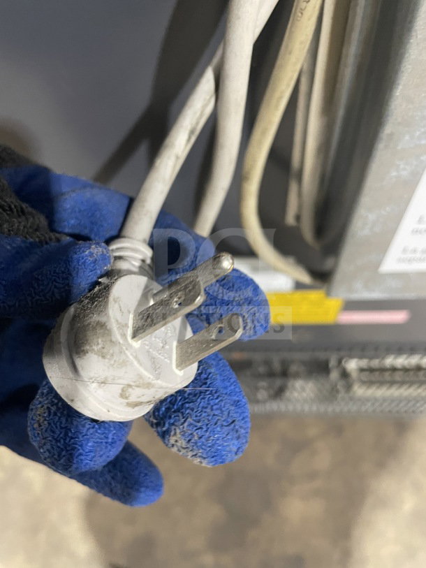 Close-up of power cord plug for AHT model AC S LED refrigerated display case, 115V, with blue gloved hand holding it.
