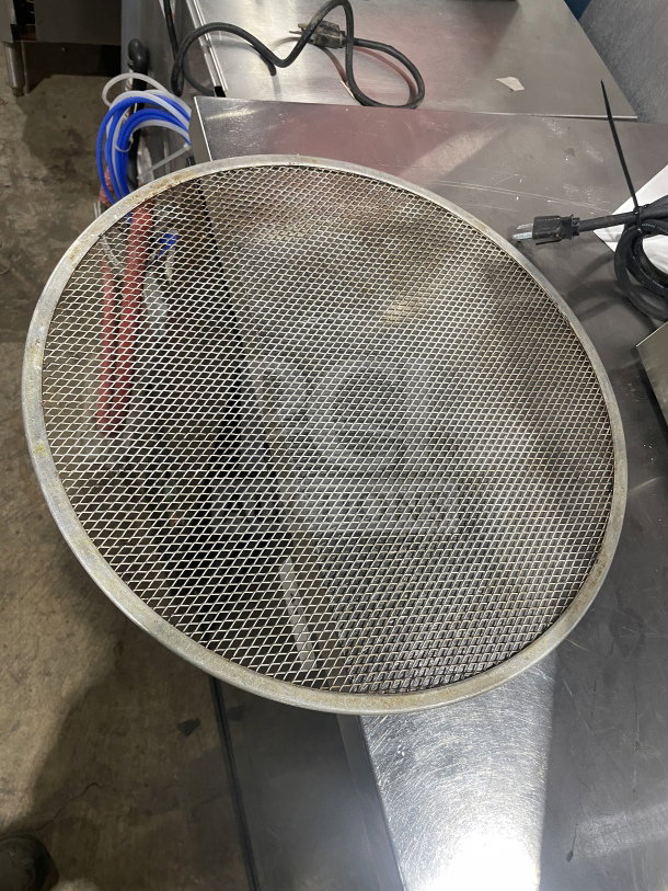 Commercial stainless steel pizza holder, heavy duty, with mesh design. Appears in used condition, showing some wear.