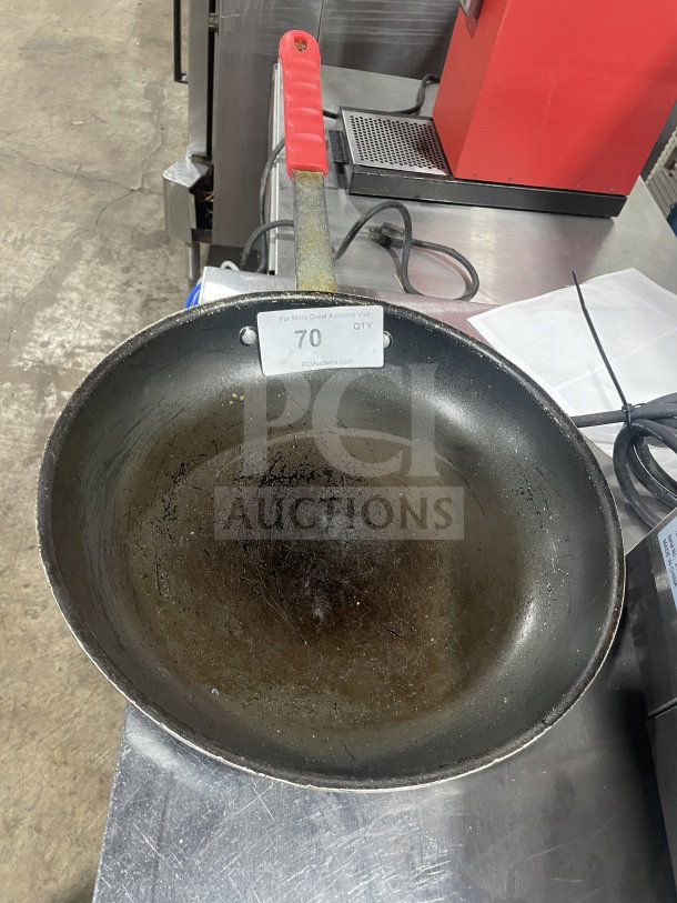 Commercial non-stick aluminum fry pan with red silicone handle sleeve, used condition, auction tag visible.