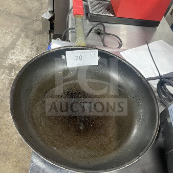 Commercial non-stick aluminum fry pan with red silicone handle sleeve, used condition, auction tag visible.