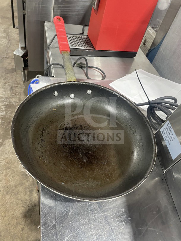 Commercial non-stick aluminum fry pan with red silicone handle sleeve. Used condition with visible wear.