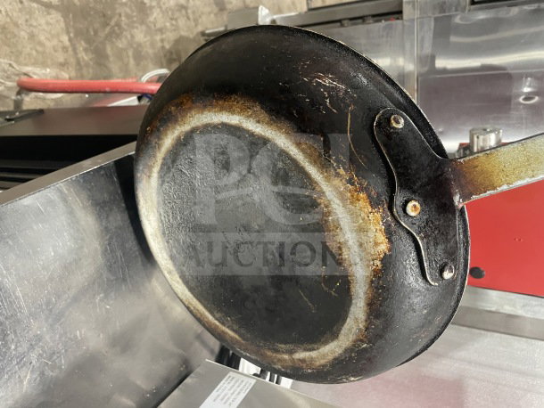 Commercial non-stick aluminum fry pan with used patina, red silicone handle sleeve, visible bottom markings indicating wear.