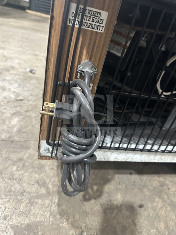 Marc refrigerated display case backside; wooden trim, poly-coated wired rack, 115V plug coiled; warranty tag visible.