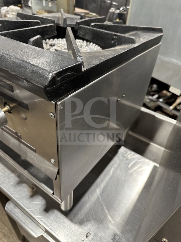 Commercial stainless steel gas stock pot range with triple knob configuration, used condition, sturdy cast iron top.