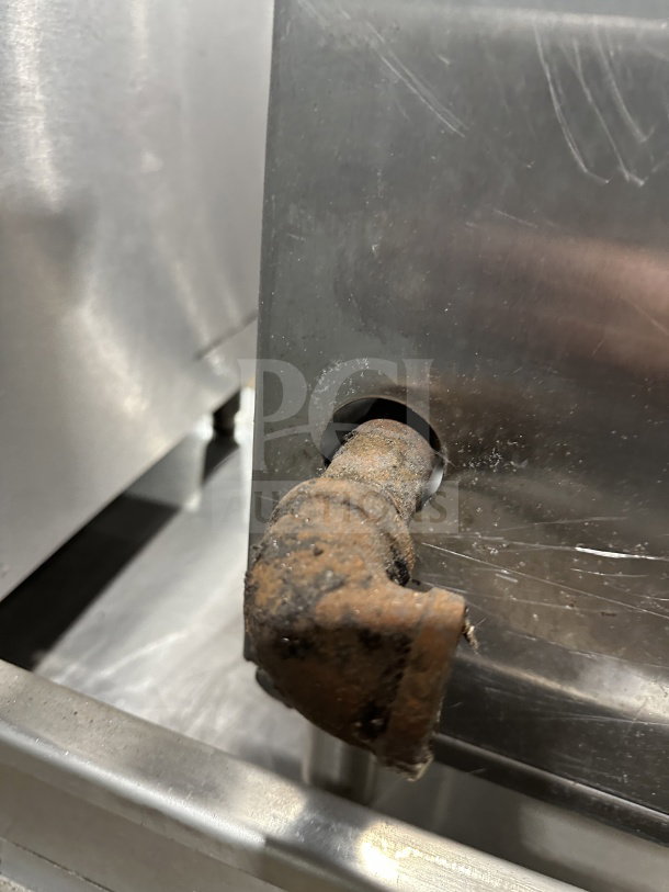 Commercial stainless steel gas stock pot range with triple knob configuration. Visible rust on pipe. Ideal for high-volume cooking.