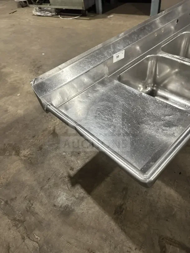 Commercial stainless steel 3-compartment sink with two side drainboards, sturdy legs, and labeled number 99. In good condition.