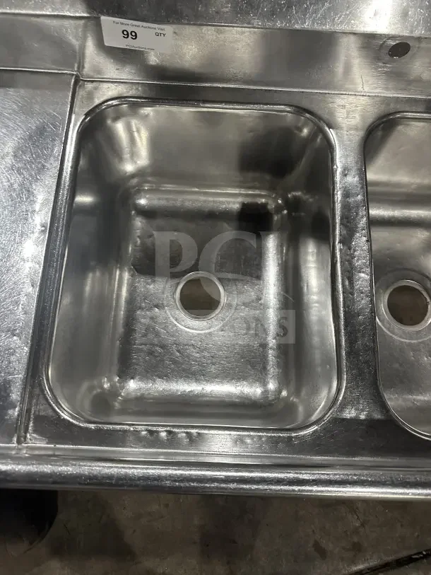 Commercial stainless steel 3-compartment sink with two side drainboards and legs. Visible auction label indicates item number 99.