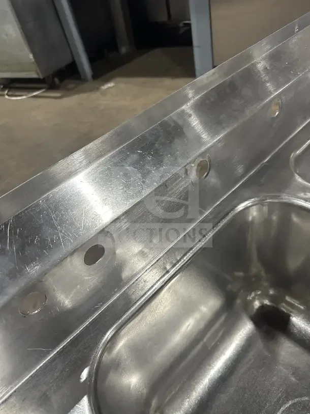 Commercial stainless steel 3-compartment sink with two side drainboards and sturdy legs, shown in clean condition.