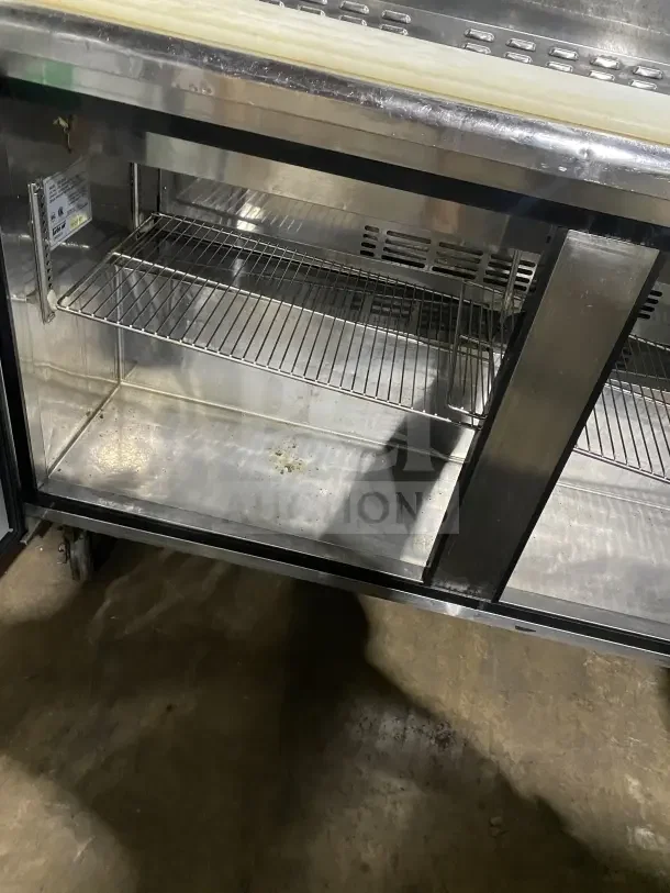Turbo Air TST60SD refrigerated prep table with chrome rack, cutting board, stainless steel finish. Model and serial visible.
