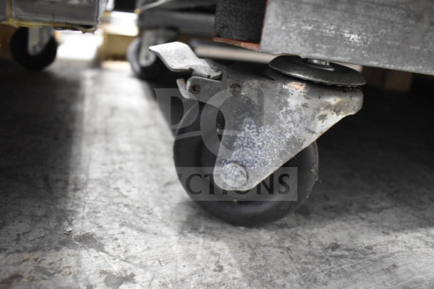 Close-up of a commercial caster on the Migali C-3FB-HC freezer, showing wear on the metal support and rubber wheel.