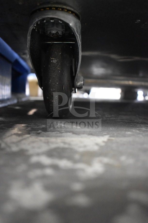 Close-up of commercial caster wheel under Migali C-3R-HC commercial 3-door reach-in cooler, model number visible.
