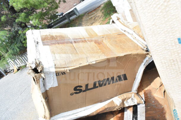 Damaged cardboard box labeled "WATTS" containing new scratch and dent items, including shelf and pot rack. Box shows signs of wear.