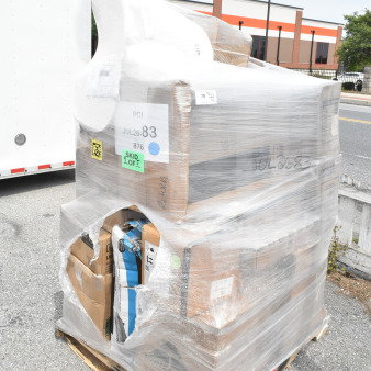 Shrink-wrapped pallet with various boxed items, labeled "JUL26-83" and "SKID 1 OF 5," including chair cushions and pendant lights.