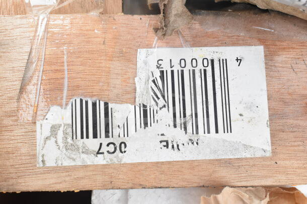 Close-up of a damaged barcode label on wood, partially torn and covered with clear tape.