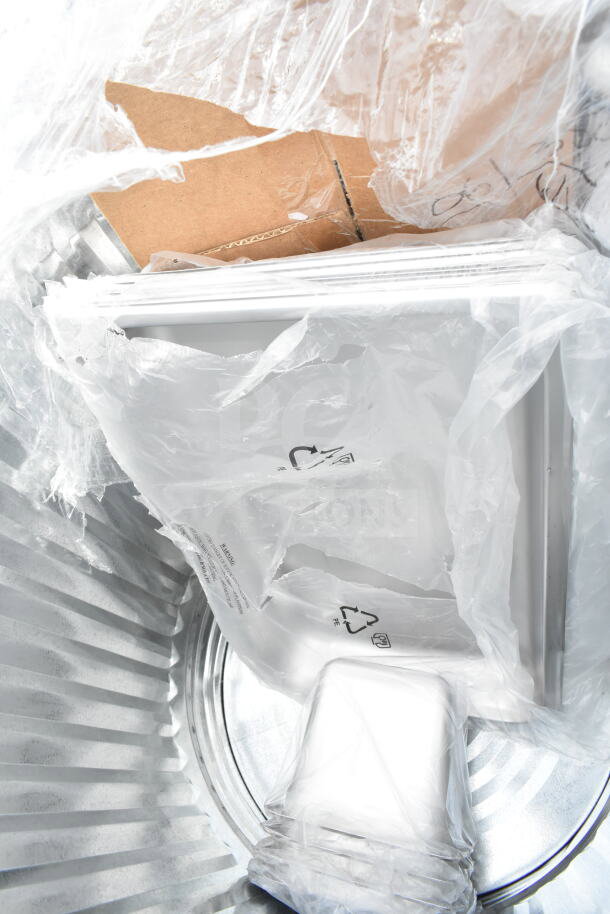 New scratch and dent items in packaging, including overshelf, tabletop, and trash can, in a metal trash bin.