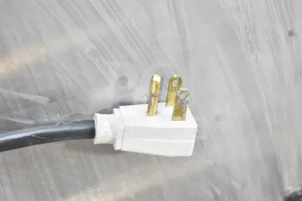 Close-up of a power plug for True TSSU-72-30MB-ST-HC prep table, showing three brass prongs and a white connector.
