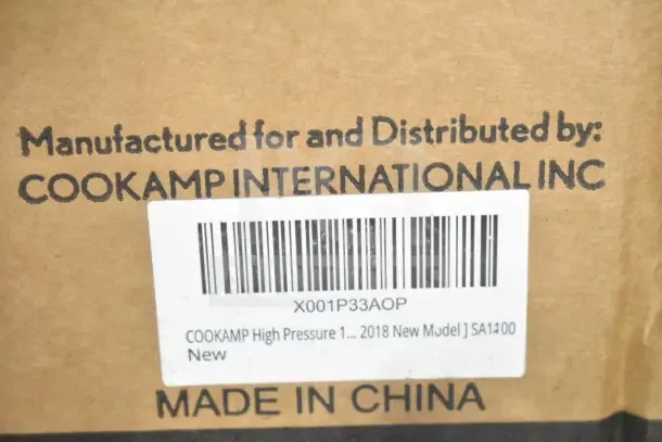 "Cookamp SA1100 High Pressure Outdoor Gas Cooker box, brand new with minor scratches and dents. Made in China. Barcode and model details visible."