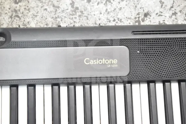 Close-up of Casiotone LK-S250 keyboard in black, showing keys and speaker grille, in good condition.