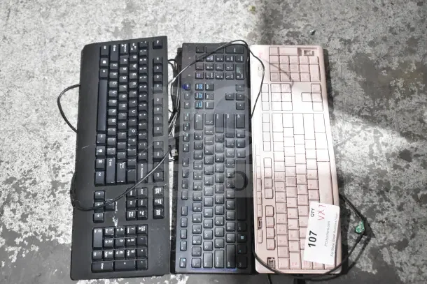 Seven assorted wired computer keyboards, mix of black and pink, varying brands, models, and conditions; auction lot tag visible.