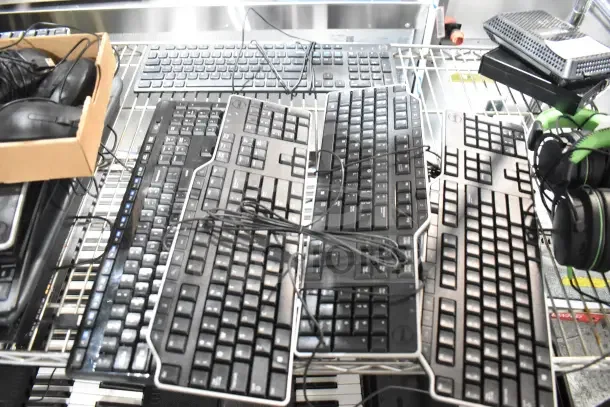 Five various computer keyboards on a metal rack, showing different brands and designs. Includes cords, mixed condition.