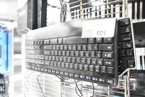 Five assorted computer keyboards, stacked on a metal rack. Includes various models in used condition. Auction tag reads "QTY 5 VXS."