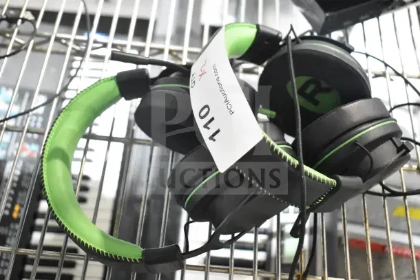 Two sets of black and green over-ear headphones on a rack. Tag marked "PCAuctions.com #110." Good condition.