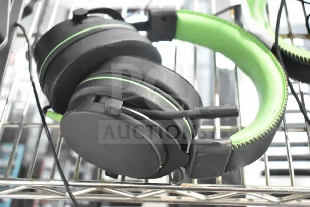Black and green over-ear headphones on metal shelf, adjustable mic. Suitable for gaming, lightly used condition.