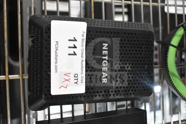 Netgear device with label showing auction details. Includes number 111 and website link. Item on metal shelf.