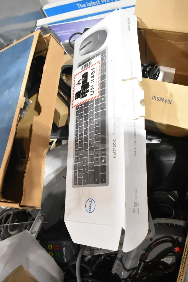 Pallet of various items including Dell KM7120W keyboard, Sensormatic ZBSMPROE box, cords, boxes, and packaging visible.