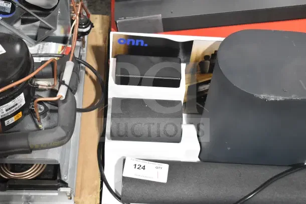 Store display featuring various Onn sound bars and speakers, showcasing sleek black designs. Auction lot tag visible.