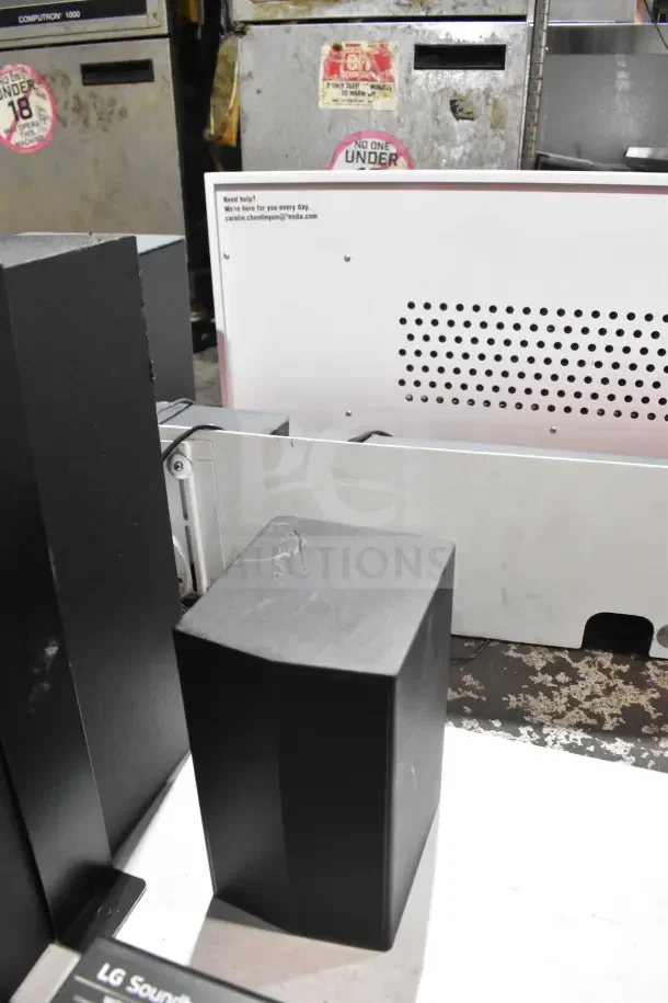 Store display featuring an LG sound bar and speakers. Black speakers, minor wear, mounted setup. Tags indicate LG branding.