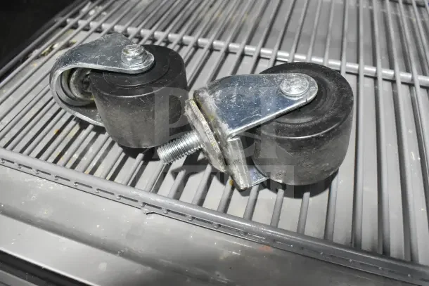 Close-up of two caster wheels on a metal grill shelf for a True T-35-HC cooler, showing metal brackets and bolts.