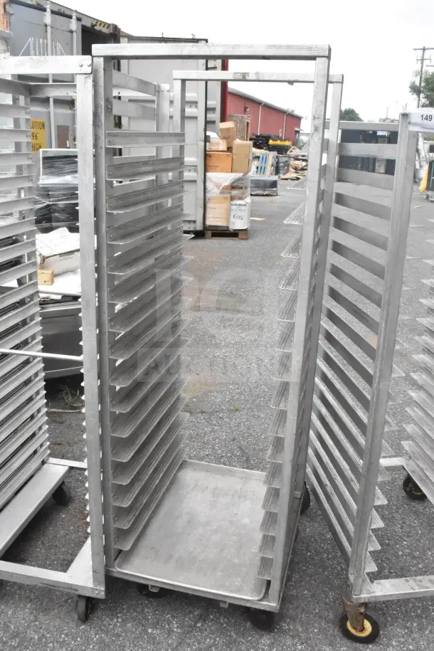 Two commercial pan transport racks on casters, silver, metal, adjustable shelves, industrial use, outdoor setting.