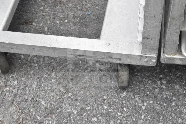 2 commercial pan transport racks with sturdy metal frames, mounted on heavy-duty commercial casters. Visible wear on frame.