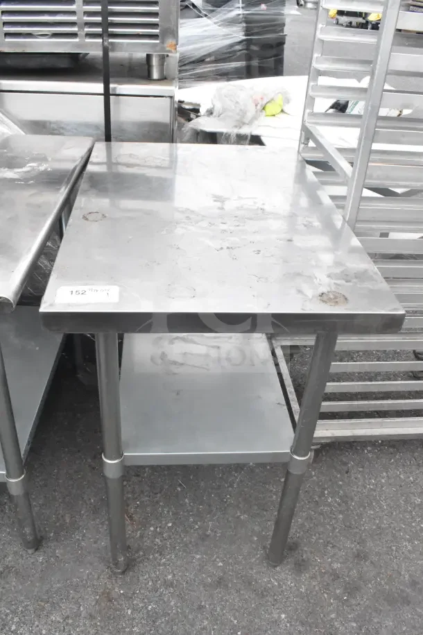 Stainless steel commercial table with under shelf, showing signs of use. Table has a visible label reading "152."