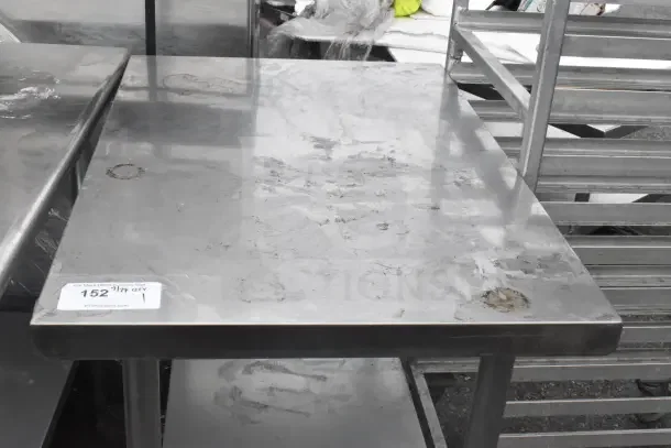 Commercial stainless steel table with under shelf, used condition, visible wear marks, label indicating lot number 152.
