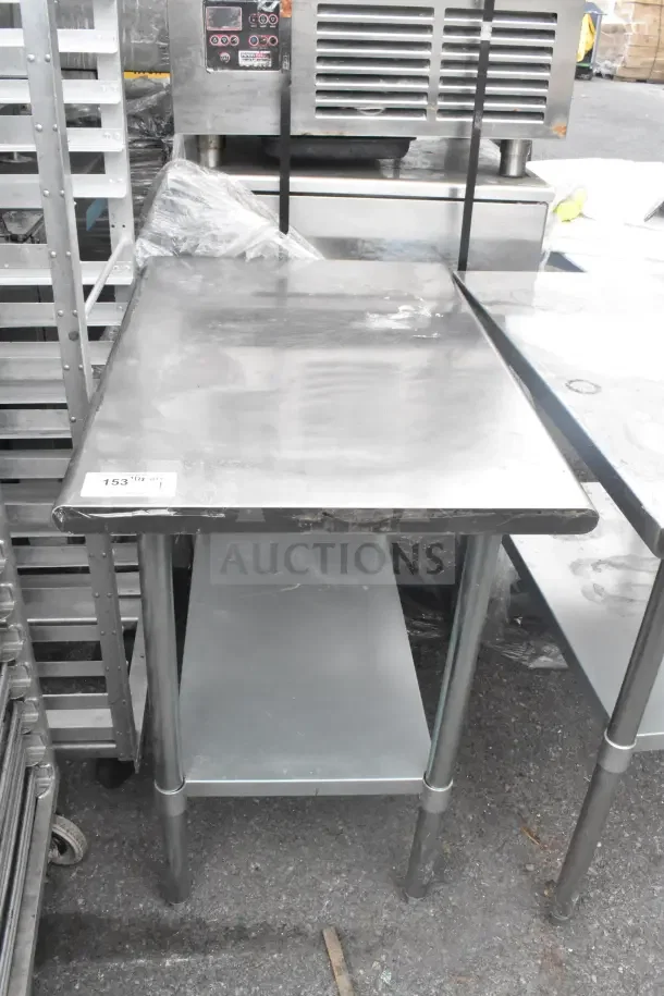 Stainless steel commercial table with under shelf, slight wear on edges, auction tag "153" visible.