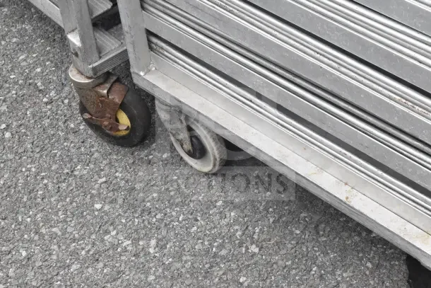 2 commercial pan transport racks on wheels, includes 56 baking pans. Visible signs of wear on racks and wheels.