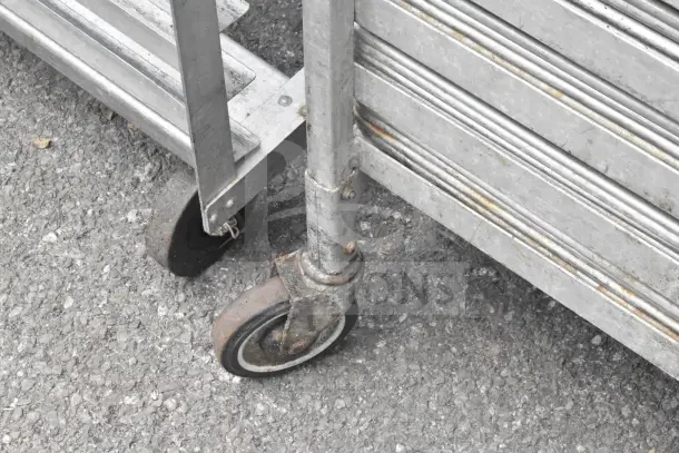 2 commercial pan transport racks with 68 baking pans, metal construction, caster wheels, some rust visible, durable.