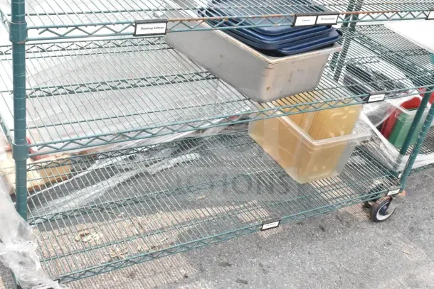 Green 6-tier wire shelving unit with bins on commercial casters. Includes labels like "Thawing Salmon." Buyer dismantles.