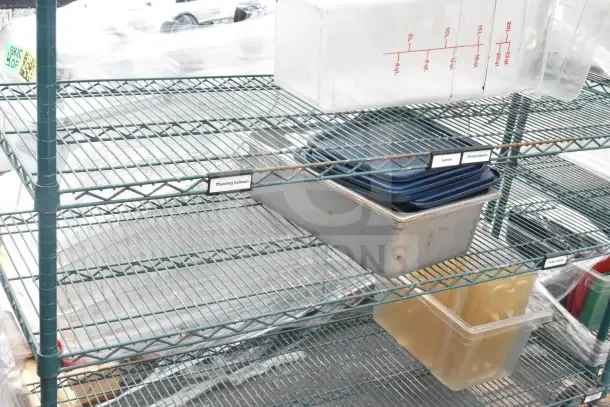 Green 6-tier wire shelving unit on commercial casters, includes plastic bins. Labels indicate various contents. Buyer to dismantle.