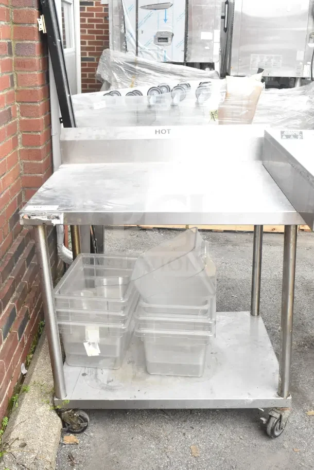 Commercial stainless steel table with under shelf, back splash, and casters. Shows wear. Includes storage bins.